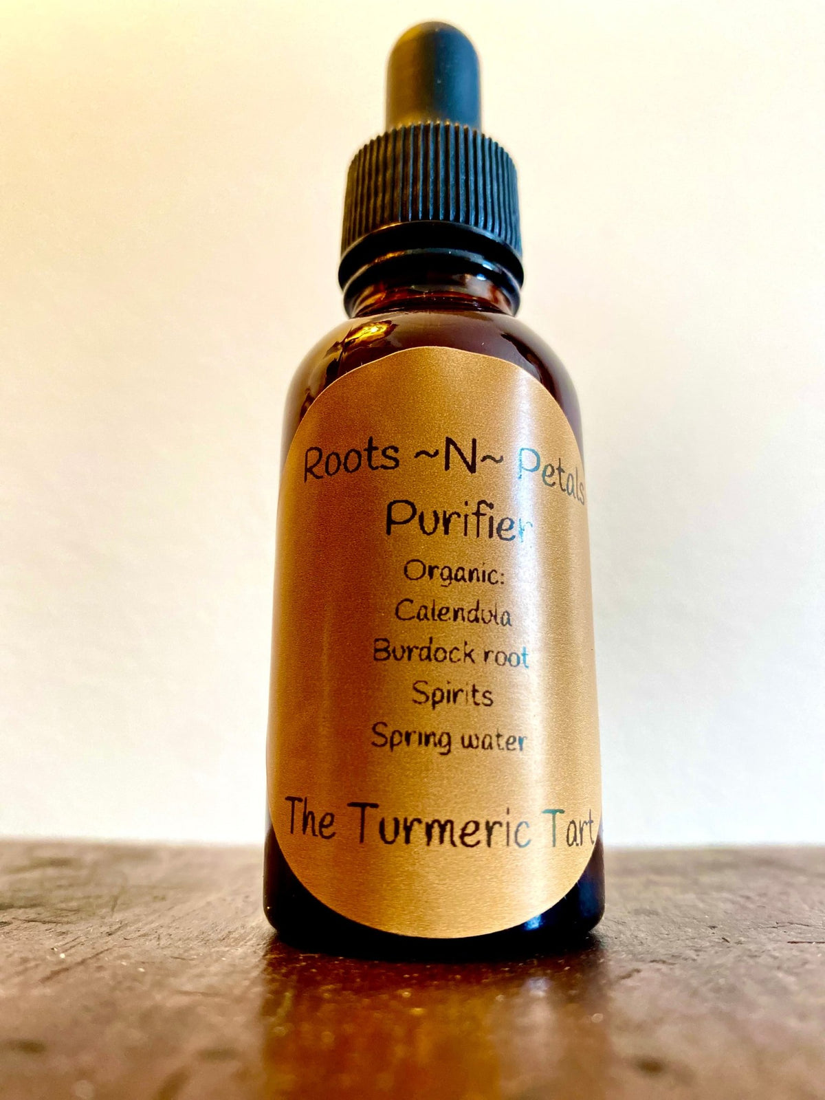 Roots~N~Petals Purifier in an amber dropper bottle with a handwritten label, on a wooden surface