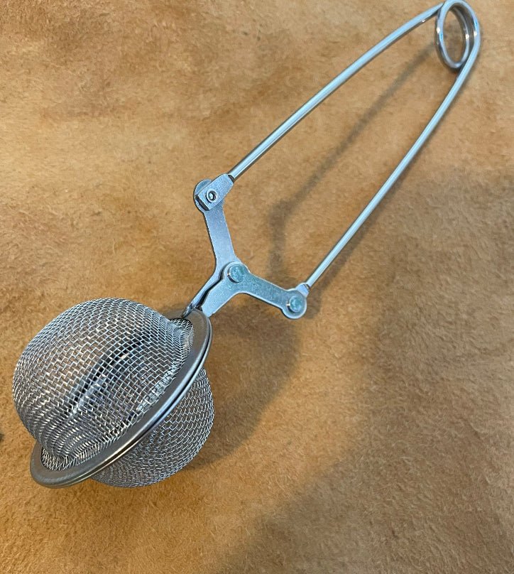 Stainless steel mesh ball loose leaf tea diffuser with a squeeze handle, on a linen cloth