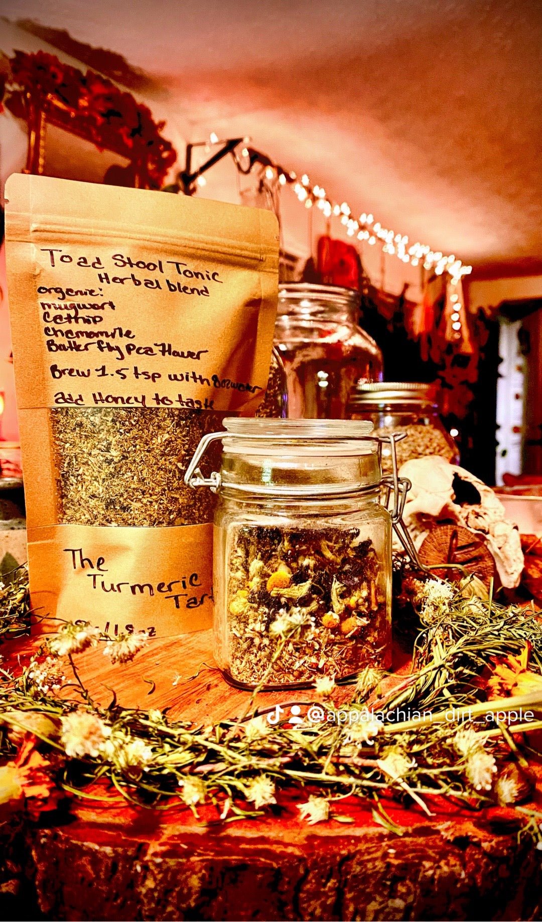 Toadstool Tonic kraft pouch beside a glass jar of the loose leaf blend, with dried flowers and string lights