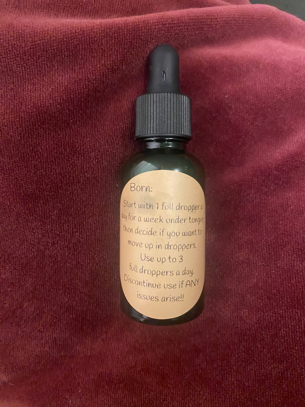 The Monthly Ally dropper bottle on a burgundy fabric background with its label visible